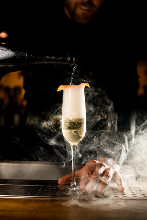 Close-up of wineglass with carbonated drink and bartender pouring liquid from bottle into glass