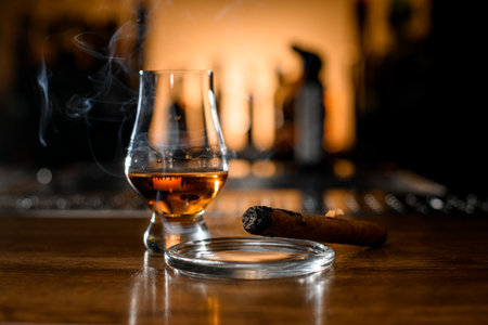 Selective focus on smoking cigar and glass with whiskey on blurred bar backgroundの写真素材