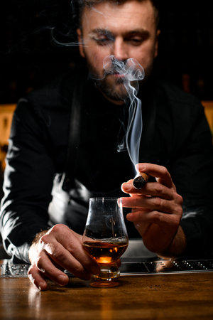 amazing view on smoking cigar in the hand of a male bartender and a glass of cognacの写真素材