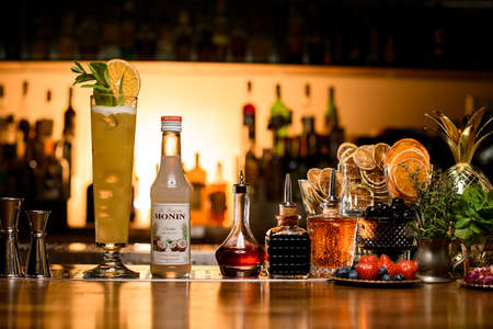 UKRAINE, KYIV - DECEMBER 06, 2021: close-up of tall glass with drink and bottle of monin syrup and variety of bar equipment on bar counterのeditorial素材