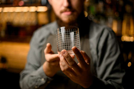 shiny empty transparent glass with pattern in the hands of male bartenderの写真素材