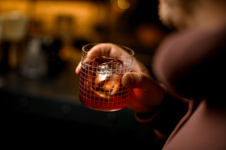 Selective focus on cocktail glass with cold drink and ice cube in male hand