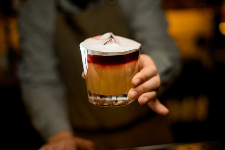selective focus on glass of colored layered cocktail with foam in male hand