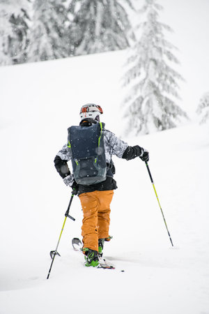 rear view of skier with backpack and hiking equipment walking at deep snow