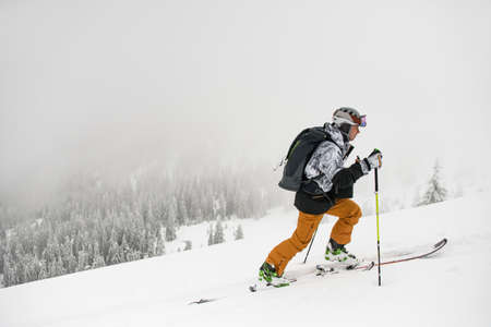 Side view of male skier with trekking poles climbing up snowy mountain slope.の写真素材
