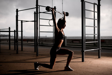 healthy woman standing with bent knees and holding barbell with her arms outstretched.の写真素材