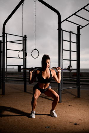 front view on young athletic woman standing on bent knees and holding barbell on her shoulders.の写真素材