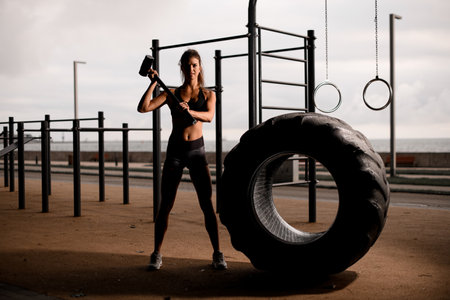 great view on athletic woman with sledgehammer stands near big tireの写真素材