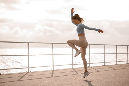 young energy woman with perfect fit body in sports clothing jumping outdoors. Side view.の写真素材
