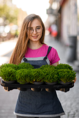 Portrait of woman holding tray with green plants growing in potsの写真素材