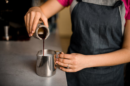 Female hand carefully pours coffee from grey measuring cup into metal jugの写真素材