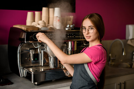beautiful woman barista stands at coffee machine and prepares drinkの写真素材