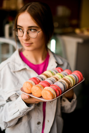 Focus on fresh french macarons on tray in hands of handsome young woman.の写真素材