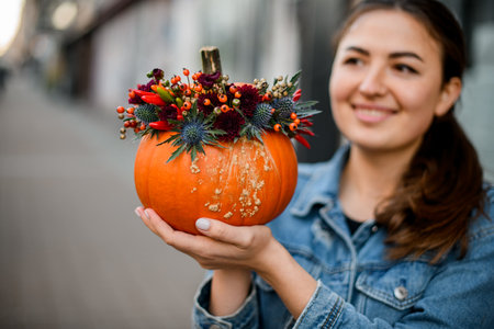 beautiful autumn arrangement of flowers berries and pepper in round pumpkin on hands of woman.の写真素材