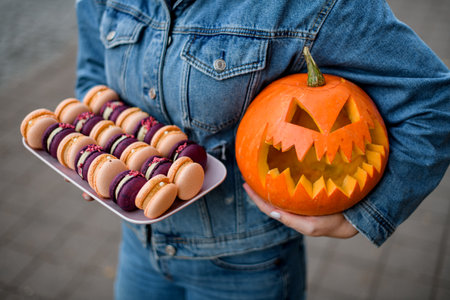 view of sweet macarons on tray and pumpkin carved with scary laughing face in the hands of womanの写真素材