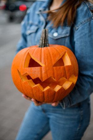 Close-up of beautiful bright orange pumpkin with carved smiling face in female handsの写真素材