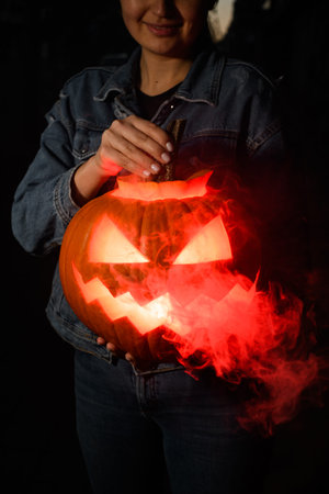 Close-up of handmade halloween pumpkin with burning and smoking mouth and eyes in female hands. Jack-o-lanternの写真素材