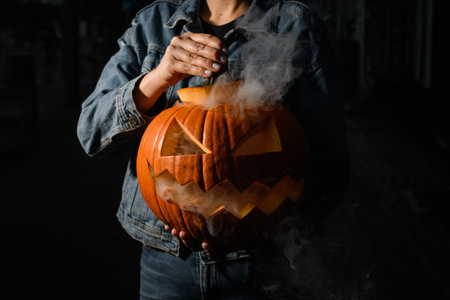 great pumpkin with carved eyes and mouth and smoking from the inside in the hands of womanの写真素材