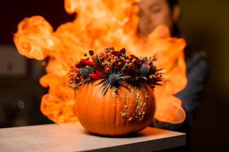 Close-up of bright orange pumpkin with flower berries and peppers in it against the background of fiery flameの写真素材