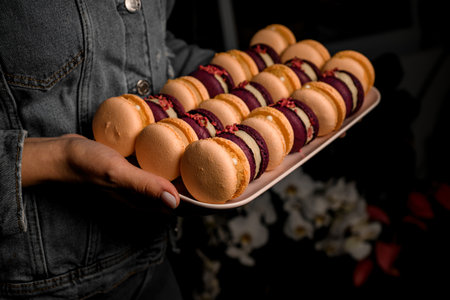 Tasty macarons cakes of different colors on tray in female hands.の写真素材