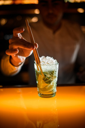 close-up of glass with iced mojito and hand of bartender inserts drinking straw in glassの写真素材