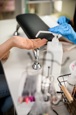 Close-up view of female hand under at dispenser bottle and hands in gloves pushing itの写真素材