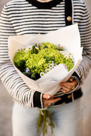 close-up of bouquet of curly green and small white chrysanthemums in wrapping paper in female handsの写真素材