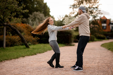 Young man and woman whirling holding by hands at park.の写真素材