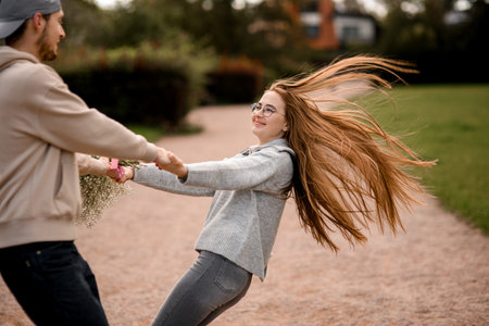 Happy young woman and man look at each other and whirling holding by hands