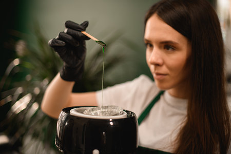 selective focus on green wax for depilation flowing down from stick in gloved hand .の写真素材