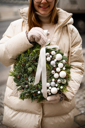 cropped photo of woman with Christmas wreath of spruce and thuja branches decorated with white balls and ribbonの写真素材