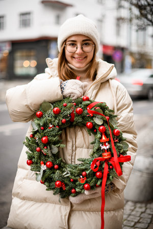 happy woman holds wreath of spruce branches and eucalyptus leaves decorated with red balls and beadsの写真素材