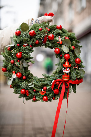 Female hand is holding of wreath of spruce branches and eucalyptus decorated with red balls and beads.の写真素材