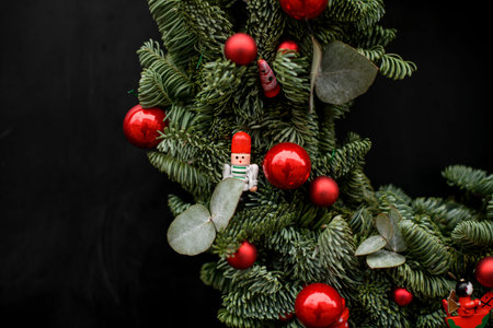 close-up view of fragment of fir wreath with red balls and red ribbon on dark background