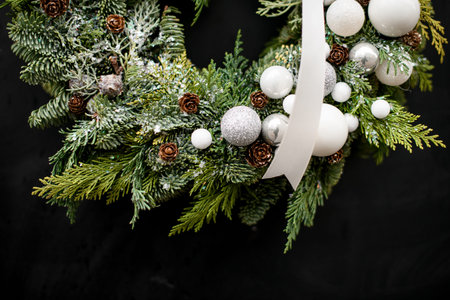 cropped photo of round wreath of spruce and thuja branches decorated with white balls and ribbon