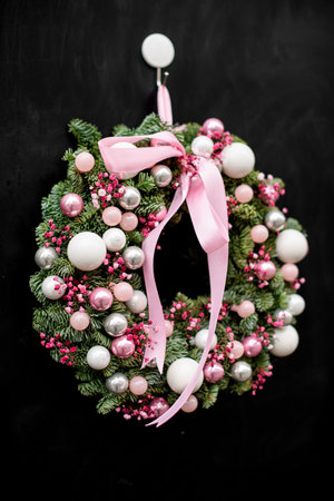 Close-up view on beautiful round wreath of fir branches decorated with pink glitter balls and flowers and bowの写真素材