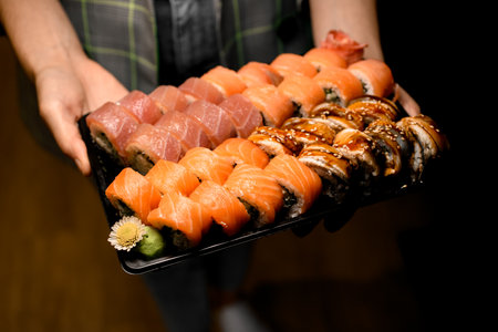 Sushi set of various philadelphia rolls with salmon, tuna, eel in black box in male hands.の写真素材