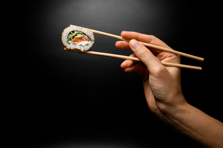 great view of sushi roll california with salmon in hand holding with bamboo chopsticks on dark background.の写真素材