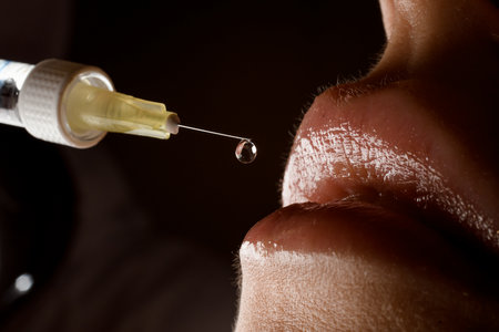 close-up view of syringe needle with drop of the drug near the female lips. Lip augmentation.の写真素材