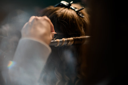 Close-up hand stylist curls long female hair with curling iron and makes stylingの写真素材