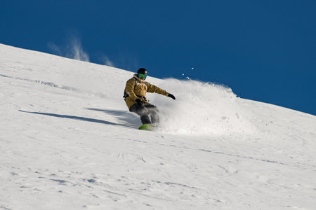 male snowboarder skilfully descends down a snowy mountain slopeの写真素材