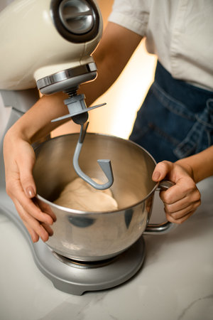 close-up of bowl that is held by female hands at the kitchen machine mixer
