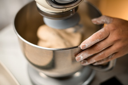 selective focus on female hand in flour at stainless bowl of modern kitchen mixer.の写真素材