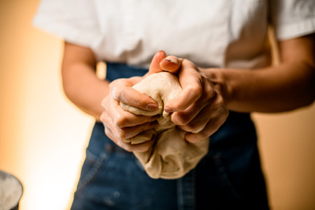 Selective focus on female hands and fingers which masterfully and vigorously knead raw bread dough