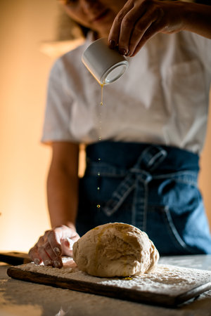 female hand pours oil from on dough on a wooden cutting boardの写真素材