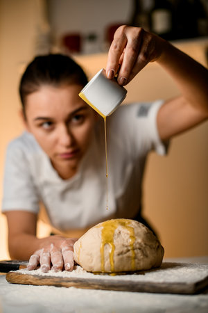 selective focus on dough on cutting board with flour and female hand accurate pours oil from a cup onto it.の写真素材