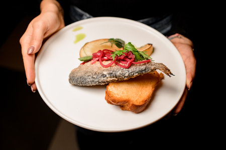 view on plate with delicious fried fish garnished with onion and lemon and toast in female handsの写真素材