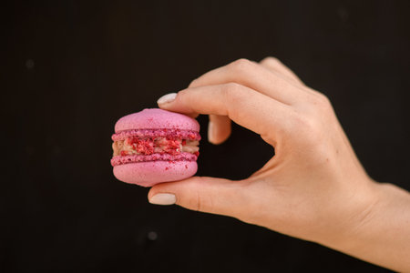 beautiful close-up of female hand holds delicious sweet pink macaronの写真素材