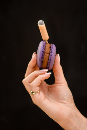 close-up view of female hand holding delicious purple macaron on black backgroundの写真素材