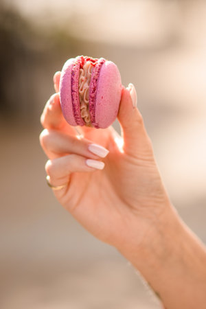 great close-up view of female hand holds delicious bright pink macaron on blurred backgroundの写真素材